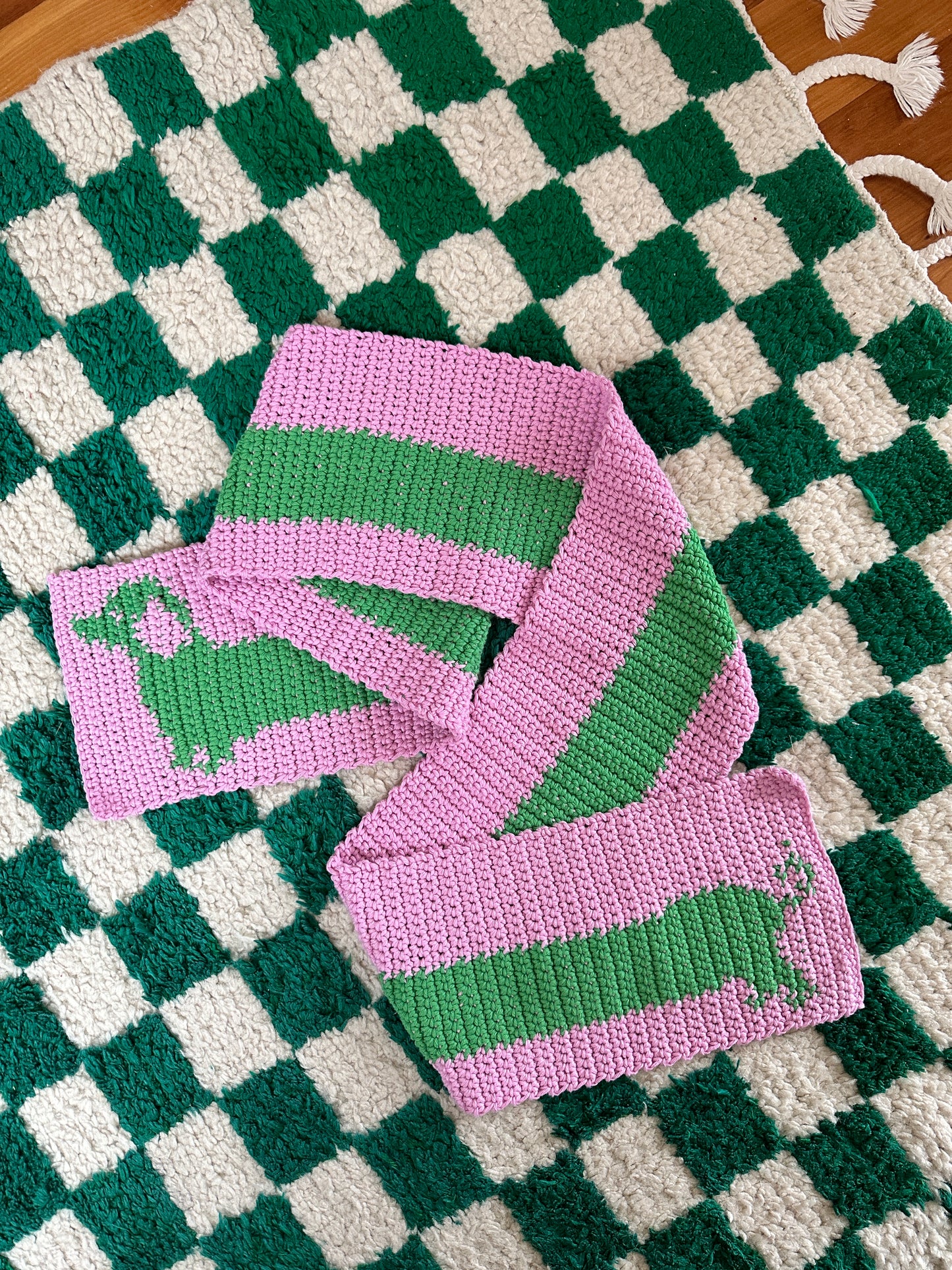 A hand touches a knitted devouthand Ready-to-order ✧ Handmade Sausage Dog scarf with wide blue stripes, draped over a dark green table. Nearby are a pen, decorative mug with brushes, and an open organizer.